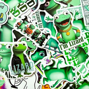 Puede incluir: Una colección de pegatinas de vinilo con lagartos verdes en varias poses y atuendos. Una pegatina muestra un lagarto con una chaqueta vaquera con el texto LIZARD HAS GREAT JEANS, y otra un lagarto con una cadena de oro y el texto I'm Lizard.
