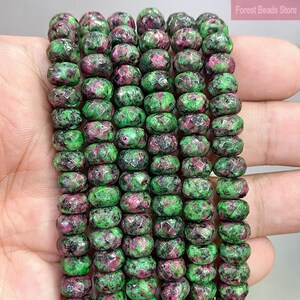 May include: A strand of faceted round beads featuring a mottled pattern of vibrant green zoisite and deep magenta ruby inclusions. The beads are arranged in multiple vertical rows, showcasing a polished texture and natural color variations.