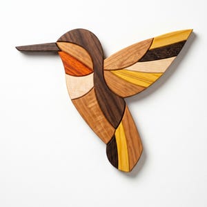 Op de afbeelding: Een wandsculptuur in de vorm van een kolibrie, gemaakt van verschillende houtsoorten. De vogel heeft een lange, donkere snavel en een lichaam dat bestaat uit in elkaar grijpende houtsegmenten in tinten donkerbruin, lichtbruin, oranje en felgeel.