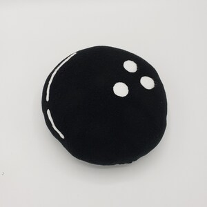 May include: Black plush toy shaped like a bowling ball with three white dots.