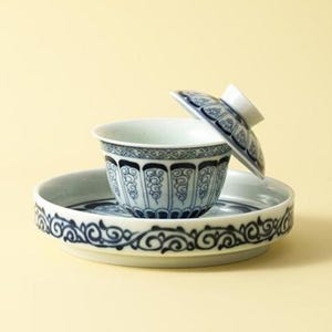 Könnte beinhalten: Eine Teetasse aus Keramik mit passender Untertasse und Deckel, die eine weiße Basis mit komplizierten blauen Blumen- und Rankenmustern aufweist. Die Tasse steht mittig auf der runden Untertasse, während der Deckel schräg am Rand lehnt.