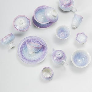 Peut inclure: Un service à thé composé de plusieurs pièces avec un émail cristallin dans des tons lavande, bleu clair et blanc. La collection comprend des théières, des bols avec couvercle, des soucoupes et des petites tasses, tous à texture craquelée.