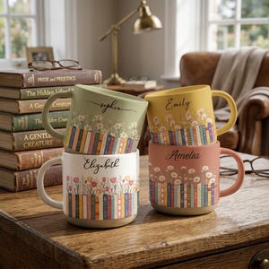May include: Four ceramic mugs with speckled finishes, each featuring a unique color, a row of illustrated books at the base, floral designs above the books, and a name printed in script: Sophia, Emily, Elizabeth, and Amelia.