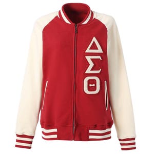 May include: A red and cream varsity jacket featuring a full-length front zip, ribbed collar, cuffs, and hem with striped detailing. The left chest displays large, white, textured Greek letters Delta, Sigma, and Theta in a vertical arrangement.