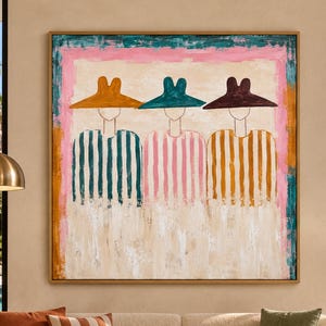 May include: A square wall painting featuring three stylized figures wearing wide-brimmed hats in orange, teal, and dark brown. The figures wear striped shirts in matching colors against a cream background with a pink and teal border frame.