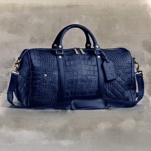 Könnte beinhalten: Eine dunkelblaue Reisetasche mit einer strukturierten Krokodilleder-Optik. Die Tasche verfügt über zwei Tragegriffe, einen abnehmbaren Schultergurt mit Polsterung, silberfarbene Metallbeschläge und einen rechteckigen Gepäckanhänger an der Seite.