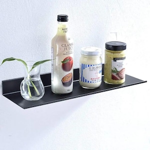 May include: A matte black metal floating wall shelf holding a clear glass vase with green leaves, a bottle of Classic Juice apple and passion fruit juice, a jar of Kewpie mayonnaise, and a jar of Atkins and Potts classic bearnaise sauce.