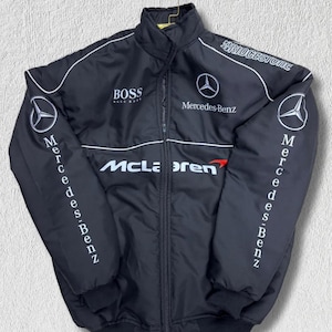 Può includere: Una giacca da corsa nera con cerniera e loghi ricamati in bianco, tra cui Mercedes-Benz, McLaren, BOSS e Bridgestone. La giacca presenta un colletto alto, maniche lunghe con polsini a coste e dettagli con profili bianchi sul petto.