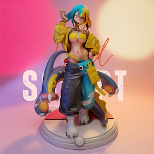 Può includere: Una statuetta in stile anime raffigurante un personaggio con capelli bicolore blu e gialli, che indossa una giacca corta gialla, un top a fascia giallo e pantaloni cargo bicolore neri e blu, in piedi su una base circolare con una creatura.