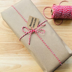 May include: A brown paper package tied with red and white baker's twine. A small brown tag is attached to the twine with the text "@ROUGHANDTUMBLEGOODS".