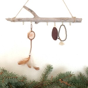 May include: A rustic wooden branch with five hooks, used as a jewelry organizer. A dreamcatcher, a brown felt leaf, and a beaded necklace hang from the hooks.