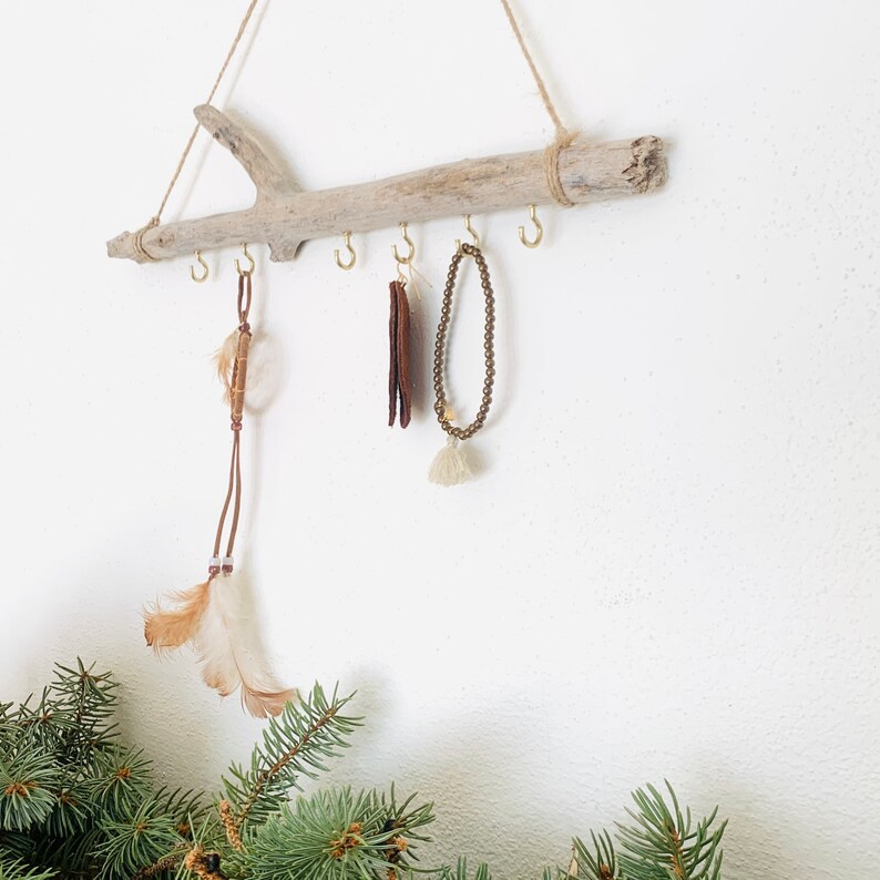 May include: A driftwood jewelry holder with five hooks and a brown leather cord with feathers hanging from one of the hooks. A brown beaded necklace hangs from another hook.