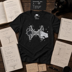 May include: A dark charcoal grey short-sleeve t-shirt featuring a white graphic print of a wormhole connecting two cats. The design includes a grid-like tunnel structure with stars and celestial elements, centred on the chest of the garment.
