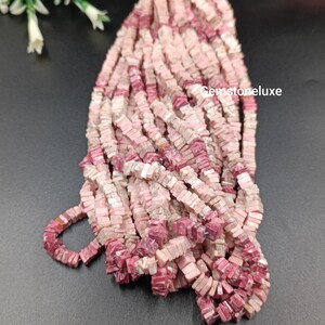 May include: A collection of small, square-shaped beads in varying shades of pink, ranging from pale blush to deep magenta, with natural white and grey veining throughout. The text Gemstoneluxe is visible on the right side of the bead strands.