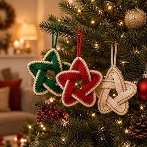May include: Three star-shaped ornaments made of crocheted yarn, each featuring a hanging loop. One star is dark green with a cream-colored border, one is deep red with a cream-colored border, and one is cream-colored with a gold-toned border.