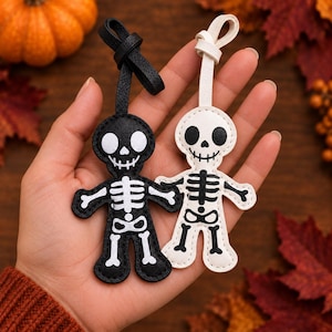 May include: Two skeleton-shaped keychains with loop attachments. One keychain is black with white skeleton details, and the other is white with black skeleton details. Both feature stitched edges and a textured surface, depicting a stylized skull and ribcage.