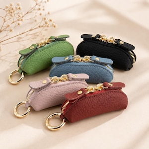 Könnte beinhalten: Eine Sammlung von fünf kleinen Schlüsselmäppchen aus genarbtem Leder in Grün, Schwarz, Blau, Rosa und Dunkelrot. Jedes Mäppchen verfügt über einen goldfarbenen Reißverschluss, eine passende Lederlasche mit goldener Niete und einen Schlüsselring.