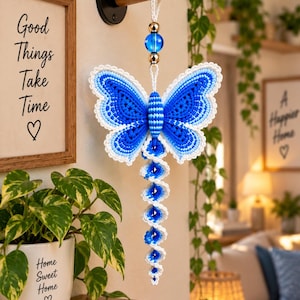 May include: A hanging macrame butterfly ornament featuring vibrant blue and white cord, accented with a central blue glass bead and metallic gold spacers. The butterfly has a spiraling tail and is suspended from a white cord loop.