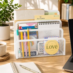 May include: A white metal mesh desk organizer with three tiered compartments holding various notebooks, a daily planner, pens, and a circular yellow sticky note with the text Love and Purrrfectly printed on the front surface.
