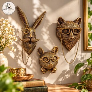 Può includere: Tre sculture da parete a forma di teste di animali con finitura oro metallizzato. Il set comprende un coniglio con monocolo, una volpe con occhiali e un topo con occhiali tondi e papillon. Ogni figura presenta dettagliate texture di pelo.