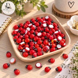 May include: A collection of small, red ladybug-shaped wooden embellishments with black spots and white adhesive backings. Many of these miniature ladybugs are contained within a square wooden tray with rounded corners, while several others are scattered on the surface.