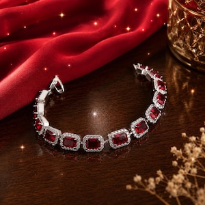 May include: A silver-toned bracelet featuring a series of rectangular, deep red faceted stones, each surrounded by a halo of small, clear white crystals. The bracelet includes a secure metal clasp mechanism and a polished finish.