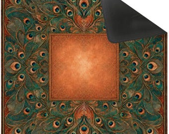 Puede incluir: Una alfombrilla cuadrada con un panel central naranja sólido rodeado por un borde detallado de patrones de plumas de pavo real en tonos verde azulado y cobre. La alfombrilla tiene esquinas redondeadas y una base negra parcialmente visible.