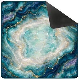 May include: A square blanket featuring a printed design of a blue and teal agate geode with crystalline textures and gold-colored veining. The fabric has a smooth surface with a folded corner revealing a solid black underside.
