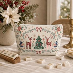 Könnte beinhalten: Eine cremefarbene Reißverschlusstasche mit festlichem Weihnachtsmotiv, bestehend aus roten Rentieren, einem grünen Weihnachtsbaum, blauen Vögeln und Blumengirlanden. Die Tasche ist mit roten Schleifen und goldenen Sternen verziert.