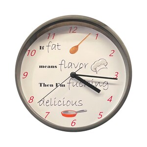 May include: A round wall clock with a dark gray frame and a white face. The clock features red numbers from 1 to 12, black clock hands, and the text "If fat means flavor Then I'm fucking delicious". Illustrations include a wooden spoon, a chef hat, and a pan.
