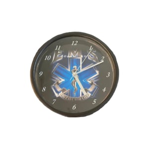May include: A round wall clock with a black frame and a black face featuring a blue Star of Life emblem. The letters E.M.S. are printed above the emblem, and the text ON CALL FOR LIFE is printed below. It has white hour, minute, and second hands.