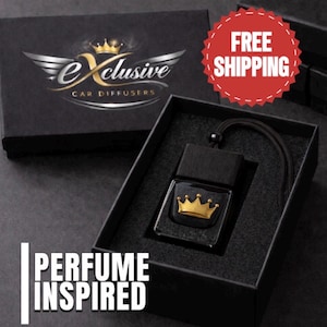 May include: A black car diffuser bottle with a gold crown emblem on the front, featuring a black wooden cap and a black hanging cord. The diffuser is presented inside a black box with the text Exclusive Car Diffusers and Perfume Inspired.