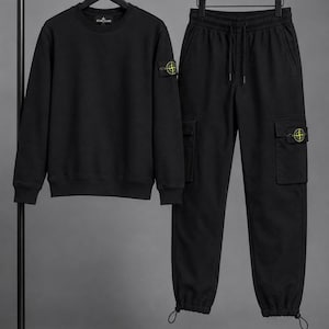 May include: A black long-sleeved crew-neck sweatshirt and matching black cargo trousers. The sweatshirt features a Stone Island patch on the left sleeve. The cargo trousers include side pockets with a matching Stone Island patch and adjustable drawstrings.