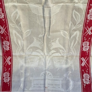 Könnte beinhalten: Vintage Leinentischdecke mit zentralem Design aus Blumen- und Korbmotiven in Weiß auf hellbeigem Hintergrund. Die Ränder haben einen roten Rand mit floralen und geometrischen Mustern und dem Wort "Rolltuch".