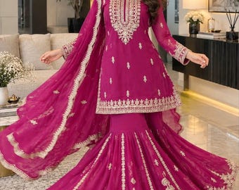 May include: A magenta three-piece ensemble featuring a long-sleeved tunic with a round neckline, a flared skirt with a wide hem, and a matching dupatta. The garment is decorated with intricate gold embroidery along the neckline, cuffs, and hem.