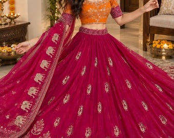 May include: A vibrant fuchsia lehenga skirt paired with a bright orange blouse. The skirt features gold embroidered floral motifs and a wide border with elephant patterns. The blouse has short sleeves with purple cuffs and intricate gold embroidery.