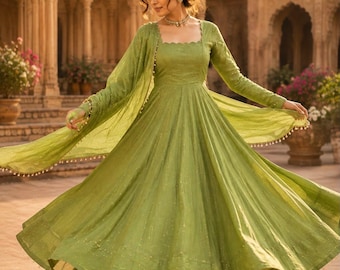 May include: A light green Anarkali dress with long sleeves, a square neckline, and a flared skirt. The outfit includes a matching sheer dupatta with small decorative beads along the edges. The fabric features a subtle, shimmering texture.