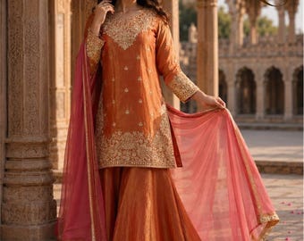 May include: A burnt orange three-piece outfit consisting of a long-sleeved tunic with gold embroidery around the neckline and hem, a matching flared skirt, and a sheer pink dupatta with a gold border. The text ZS is visible in the top right corner.