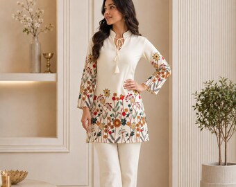 May include: An off-white tunic and matching trousers set featuring a vibrant floral embroidery pattern in red, orange, green, and brown. The tunic has long sleeves, a mandarin collar with a tie-front tassel detail, and the letters Zs in the corner.