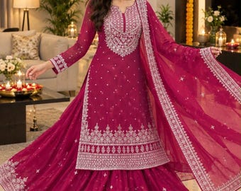May include: A magenta three-piece ensemble featuring a long-sleeved tunic with a notched neckline, a flared skirt, and a matching dupatta. The garment is adorned with intricate silver embroidery along the neckline, cuffs, and hemline.
