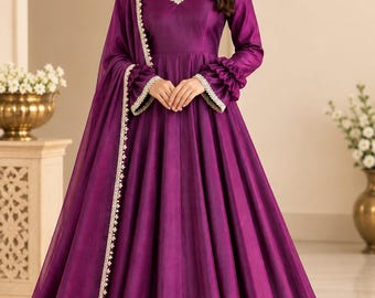 May include: A deep purple floor-length gown with long sleeves featuring ruffled cuffs, a V-neckline with white lace trim, and a matching sheer dupatta draped over one shoulder. The garment has a fitted bodice and a full, pleated skirt.