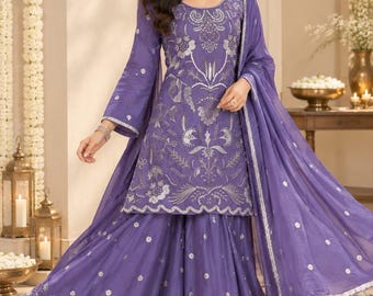May include: A purple sharara suit featuring a long-sleeved tunic and wide-leg pants with silver embroidery. The outfit includes a matching sheer dupatta with silver accents. The tunic has a round neckline and intricate floral patterns.
