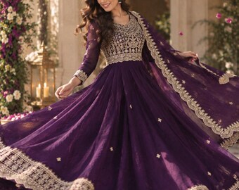 May include: A deep purple floor-length gown featuring long sleeves and a fitted bodice with intricate gold embroidery. The skirt is full and flared, accented with small gold floral motifs and a wide, ornate gold embroidered border along the hem.