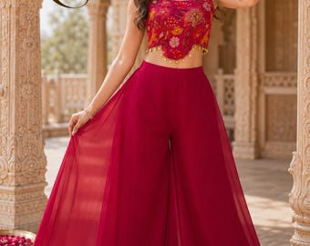 May include: A two-piece outfit consisting of a sleeveless, cropped top with a vibrant floral pattern in shades of red, orange, and yellow, featuring a scalloped hem with small gold tassels, paired with solid deep red, wide-leg chiffon trousers.