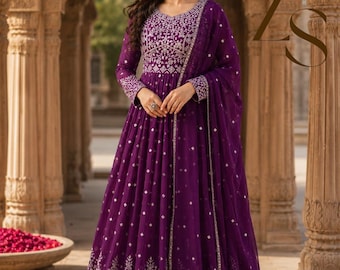 May include: A floor-length deep purple Anarkali dress featuring intricate silver embroidery on the bodice and hemline. The dress includes long sleeves and a matching sheer purple dupatta with small silver accents, creating a cohesive look.