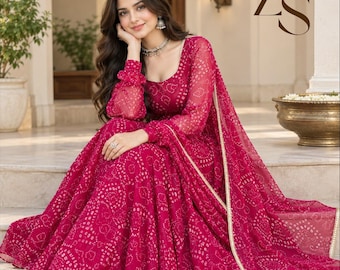 May include: A vibrant magenta floor-length dress featuring a white tie-dye pattern, long sheer sleeves with gathered cuffs, and a scoop neckline. The garment includes a matching magenta dupatta with a gold-toned border and the letters ZS.