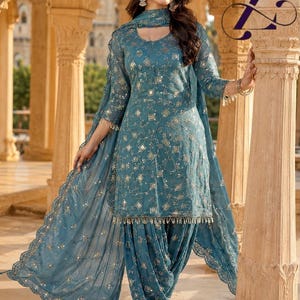 May include: A teal blue salwar kameez set featuring a long-sleeved tunic and matching pleated trousers. The fabric is adorned with intricate silver embroidery and small reflective mirror accents. A coordinating sheer dupatta with scalloped edges.