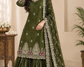 May include: An olive green three-piece ensemble featuring a long-sleeved tunic with a square neckline, a flared sharara pant, and a matching dupatta. The set is adorned with intricate silver embroidery, floral motifs, and deep red accents.