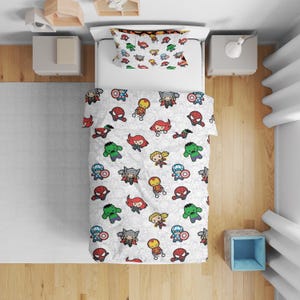Könnte beinhalten: Eine weiße Bettdecke mit passendem Kissenbezug, die ein wiederkehrendes Muster aus bunten Superhelden-Figuren im Chibi-Stil zeigt, darunter Iron Man, Spider-Man, Hulk, Thor und Captain America, vor einem dezenten, hellgrauen Linienhintergrund.