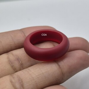 May include: A solid, smooth, matte-finish ring in a deep burgundy red colour. The interior of the ring band features the letters CGA printed in a small, white, sans-serif font. The ring has a rounded, thick profile and a simple, continuous band design.